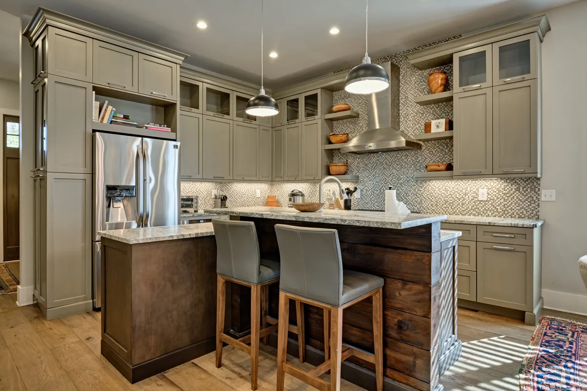 A modern kitchen with a large island, gleaming countertops, statement pendant lighting, a stylish backsplash, and stainless steel KitchenAid appliances. The design is inviting, ideal for cooking, entertaining, or enjoying a casual breakfast.