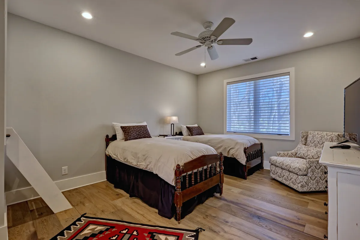 A cozy twin bedroom featuring two twin beds, a large window streaming in daylight, and a comfortable armchair for reading or relaxing. The setting is inviting and ideal for children or friends sharing a room.