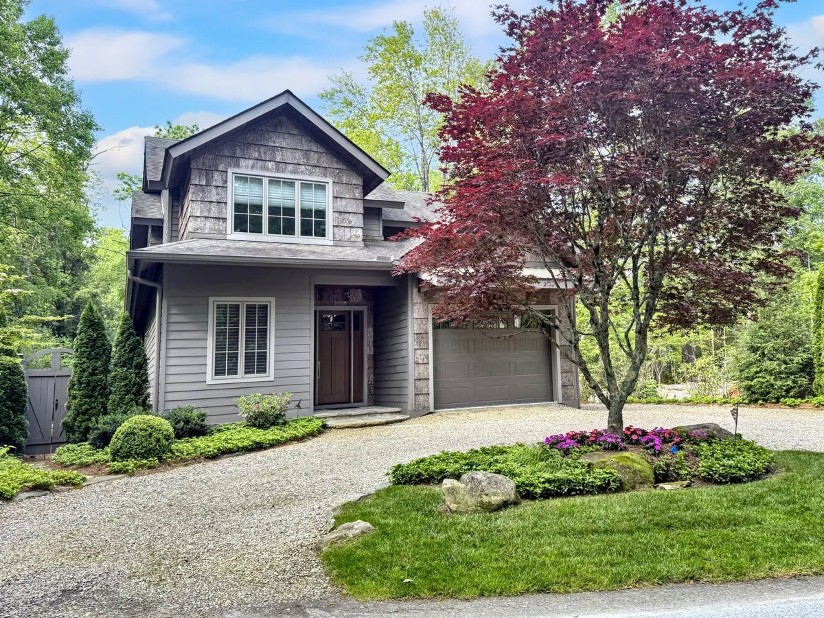 This exterior image focuses on the home's front door, with a lush flowering tree and landscaped garden in the foreground. The setup suggests a seamless transition from private home life to the vibrant neighborhood beyond, highlighting the inviting nature of the property.