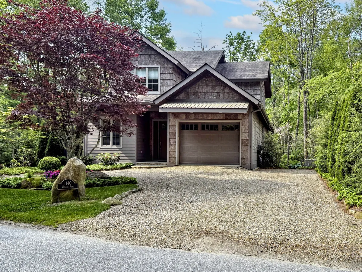 This exterior shot showcases the house's inviting facade framed by a vibrant red maple tree and a well-kept gravel driveway. The scene hints at the property's serene garden and welcoming porch, projecting both privacy and curb appeal.