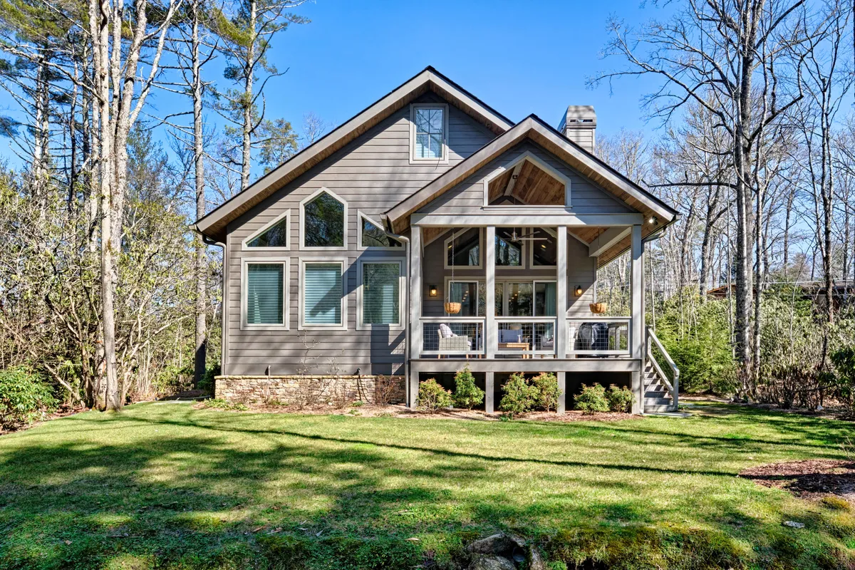 A different angle on the porch reveals its ample seating, generous covered space, and views of surrounding trees and a landscaped lawn. The inviting setup showcases how the porch is ideal for outdoor meals, morning coffee, or unwinding in the evening—emphasizing convenience and comfort close to town.