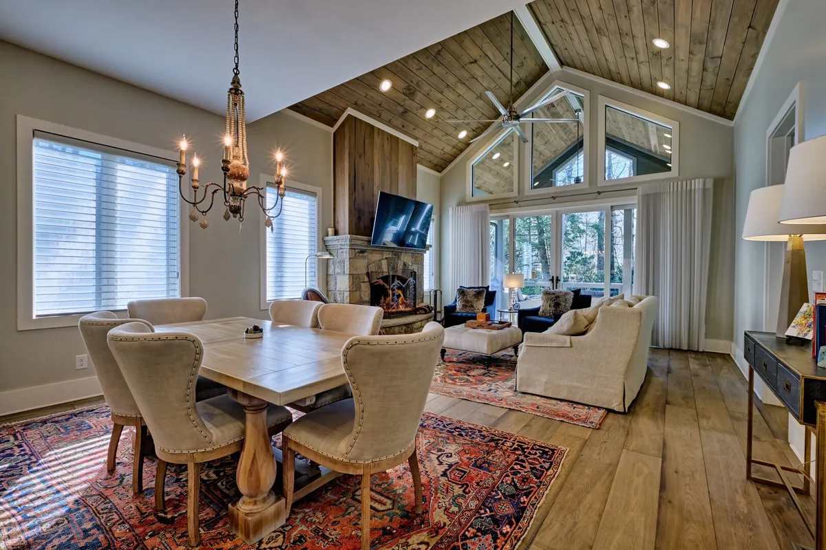 A spacious, inviting living and dining area featuring a large dining table under a modern chandelier, a cozy seating area with a fireplace, and expansive windows letting in ample natural light. The setup is ideal for both social gatherings and relaxing evenings, with a comfortable ambiance that appeals to both people and their pets.